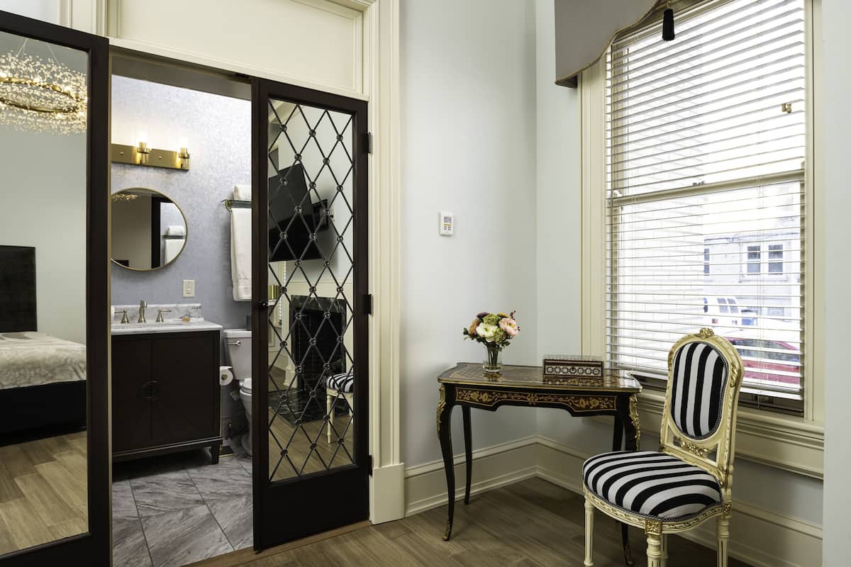 Un baño con espejo, lavamanos, inodoro y una silla decorativa.