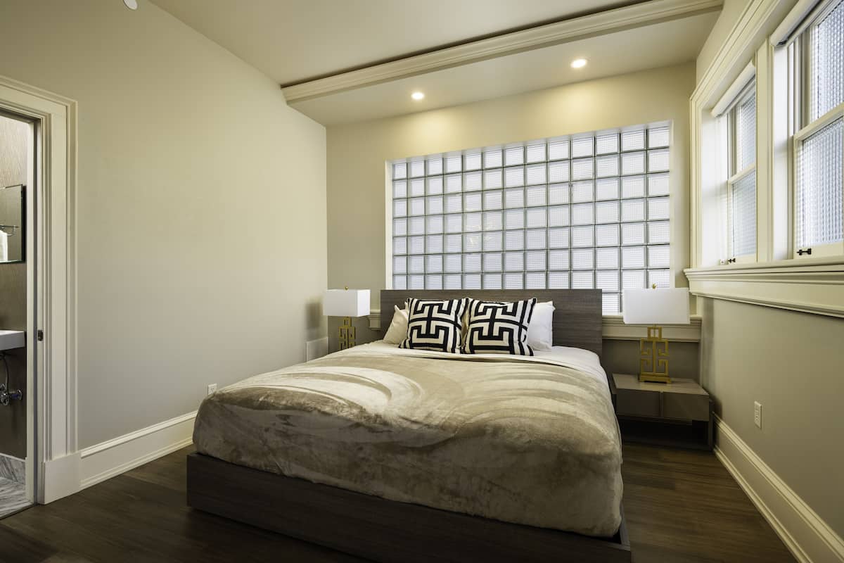 Un dormitorio con una cama grande, dos mesitas de noche con lámparas, una ventana con persianas y una puerta.