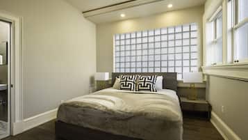 A bedroom with a large bed, two bedside tables with lamps, a window with blinds, and a door.