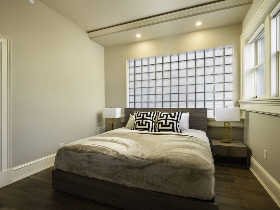 A bedroom with a large bed, two bedside tables with lamps, a window with blinds, and a door.