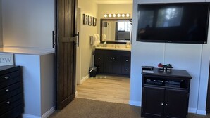 Une pièce comprenant une armoire en bois, un téléviseur fixé au mur et un coin cuisine avec un évier et un plan de travail.