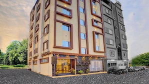 Un hotel a più piani con un negozio a livello strada, ampie finestre e un aereo visibile nel cielo.