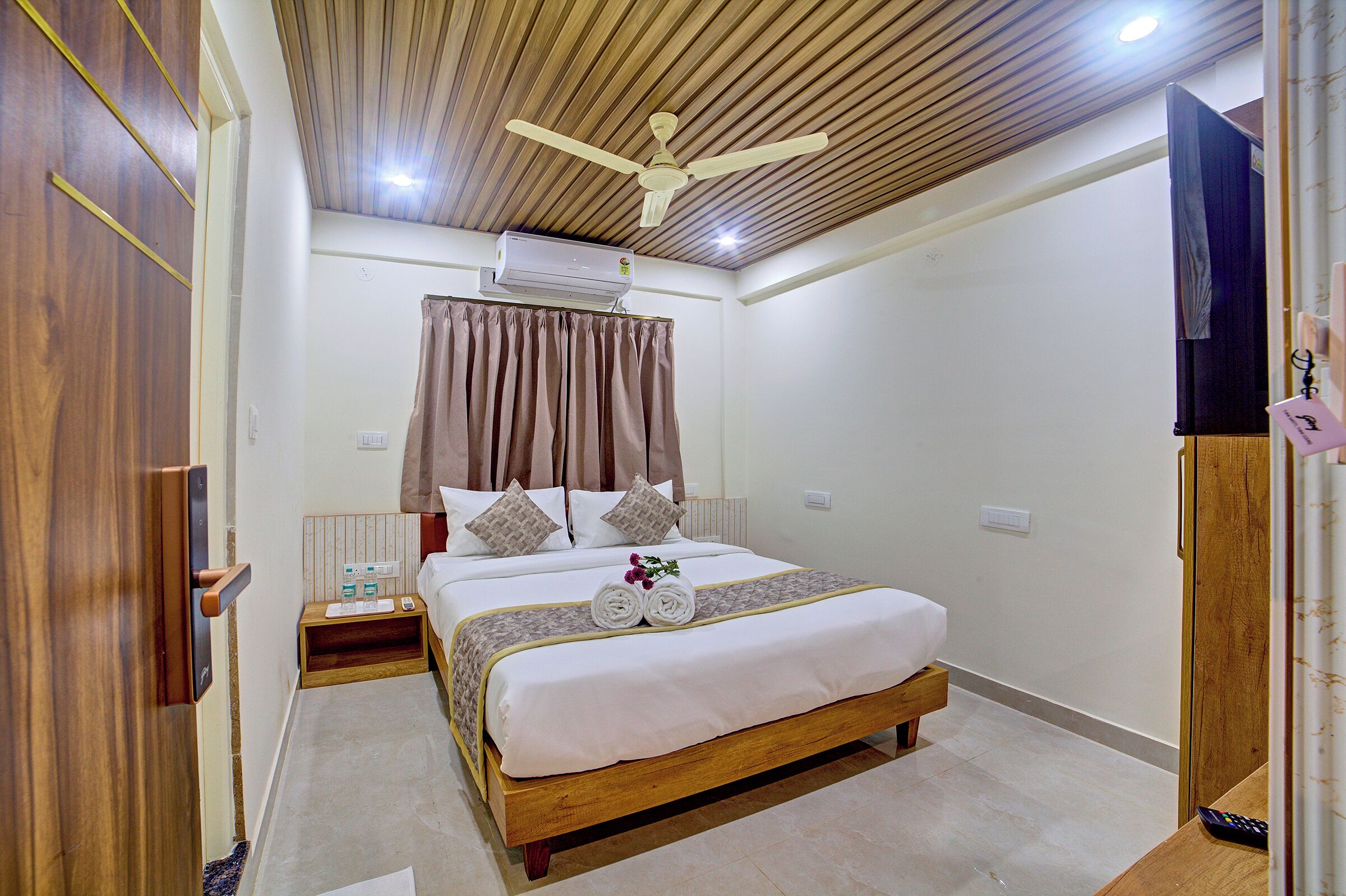 A hotel room with a wooden ceiling, a bed with a white bedspread, a nightstand with toiletries, and a ceiling fan.