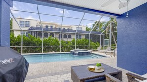 Zona junto a la piscina con una parrilla cubierta, asientos exteriores y vistas a un edificio con piscina y jacuzzi.