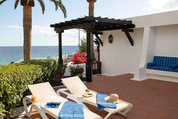 A terrace with two lounge chairs, a small table with a drink, and a blue-striped sofa.