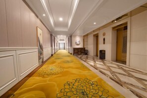 Un couloir d’hôtel avec un tapis à motifs, des œuvres d’art accrochées aux murs et un espace de réception.