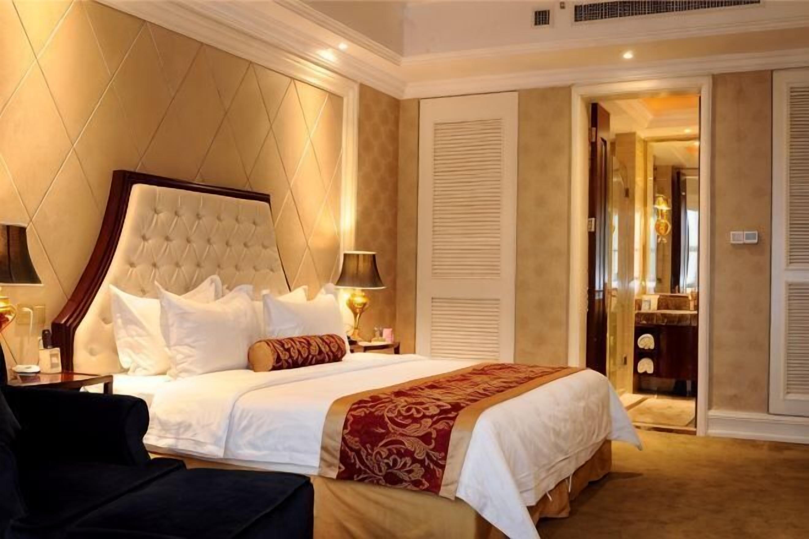 A hotel room with a large bed, bedside lamps, a nightstand, and a view of a bathroom through an open door.