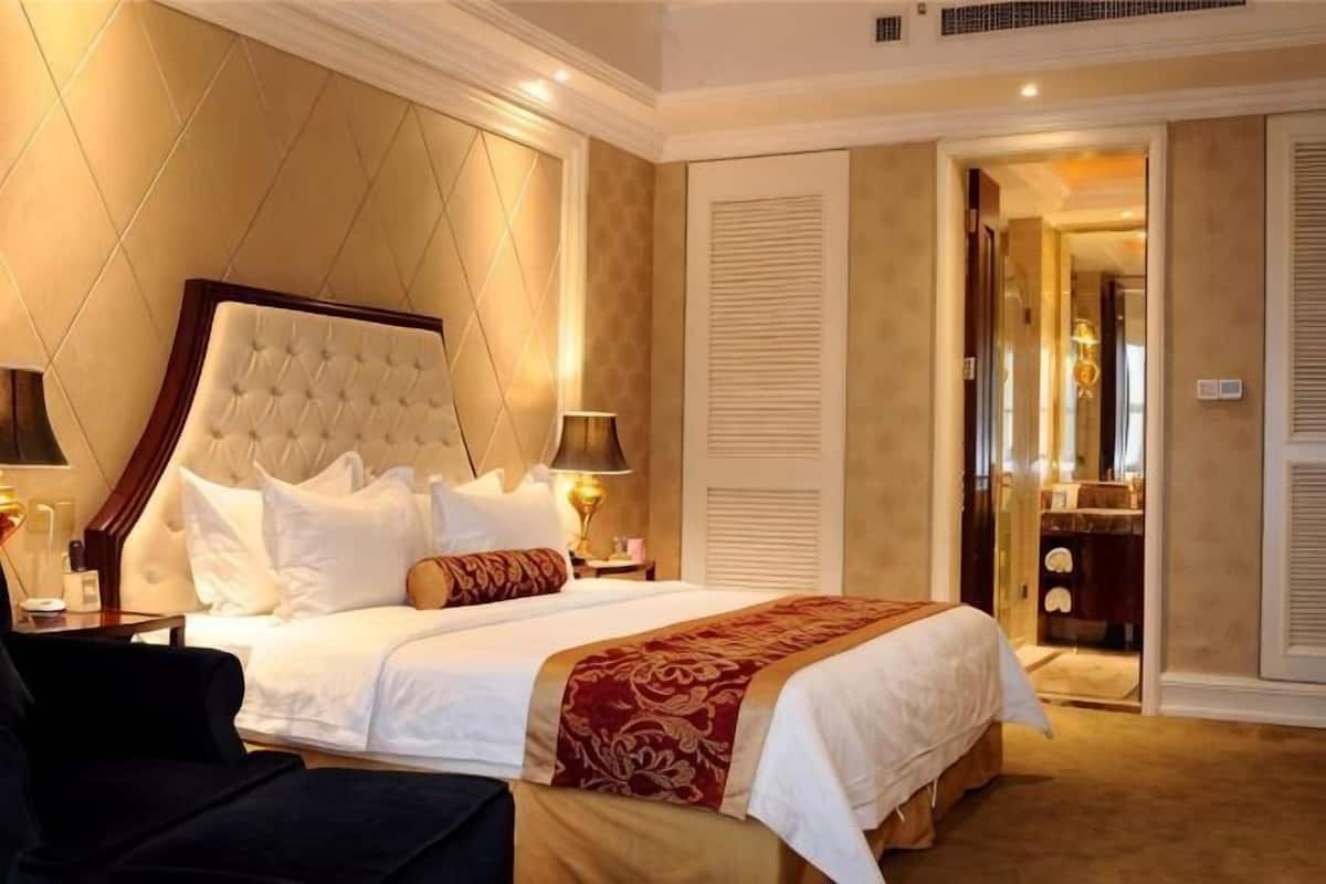 A hotel room with a large bed, bedside lamps, a nightstand, and a view of a bathroom through an open door.