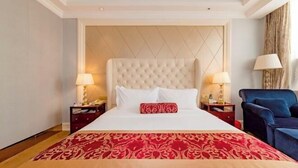 Een hotelkamer met een groot bed, twee nachtkastjes met lampen, een blauwe fauteuil en een rood-beige bedspreide met patroon.