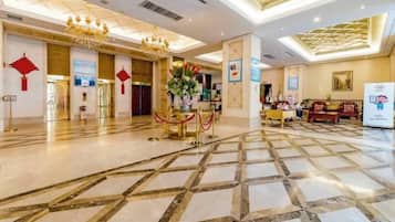 A spacious lobby with a marble floor, a reception desk, and a chandelier.