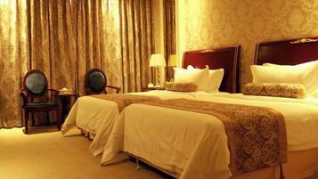 A hotel room with two beds, a sitting area with a chair, a lamp, and a large window with curtains.