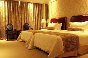 Une chambre d’hôtel avec deux lits, un coin salon comprenant un fauteuil, une lampe et une grande fenêtre avec des rideaux.