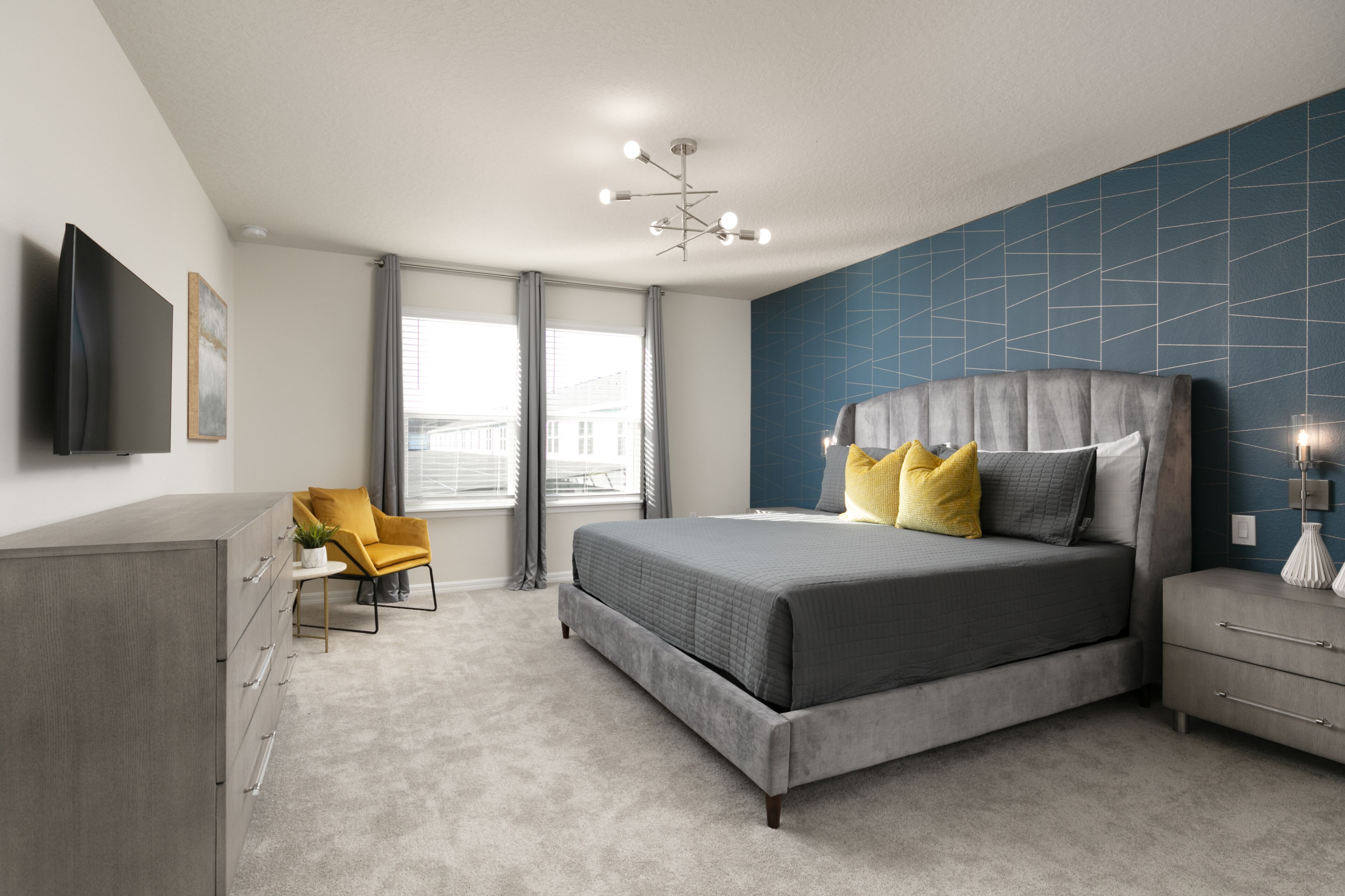A modern bedroom with a large bed, a bedside table, a chair, and a TV.