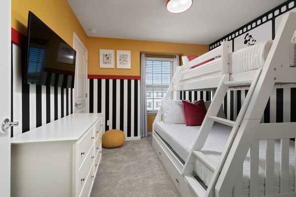 A room with bunk beds, a dresser, a television, and a window with blinds.