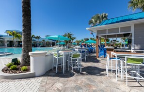 Un espace aménagé au bord de la piscine, avec des chaises longues et des parasols, un bar et une piscine.