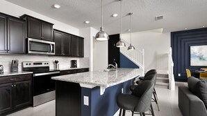 A modern kitchen with dark cabinets, a large island, and pendant lighting. - Barbecue in Summer Kitchen, Smart TV by the Pool! (Davenport)