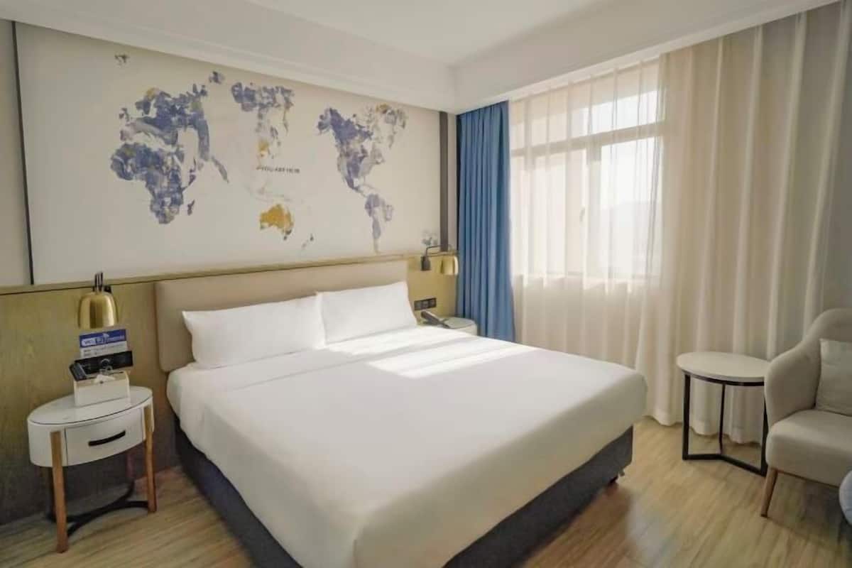 A hotel room with a large bed, a world map on the wall, a desk with a lamp, and a chair.