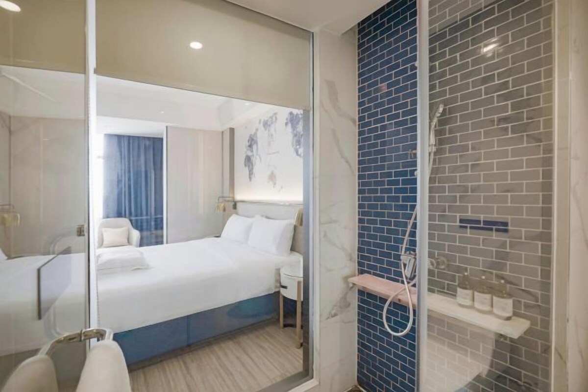 Une chambre d’hôtel avec un lit, une table de chevet, un miroir, une salle de bain avec douche et un mur recouvert de carreaux bleus.