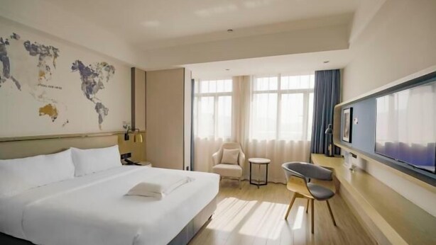 A hotel room with a large bed, a flat-screen TV, a world map on the wall, a chair, and a small table. - Kyriad Marvelous Hotel (Foshan)