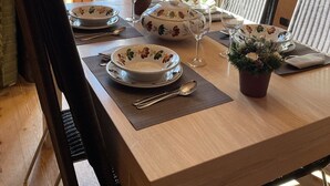 Un'area pranzo con un tavolo di legno apparecchiato per due, con stoviglie a motivi floreali e una pianta in vaso.