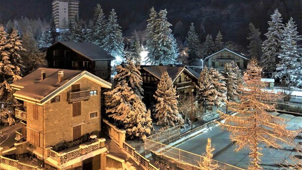 Un villaggio innevato con case di legno tradizionali, cielo sereno e una montagna in lontananza.