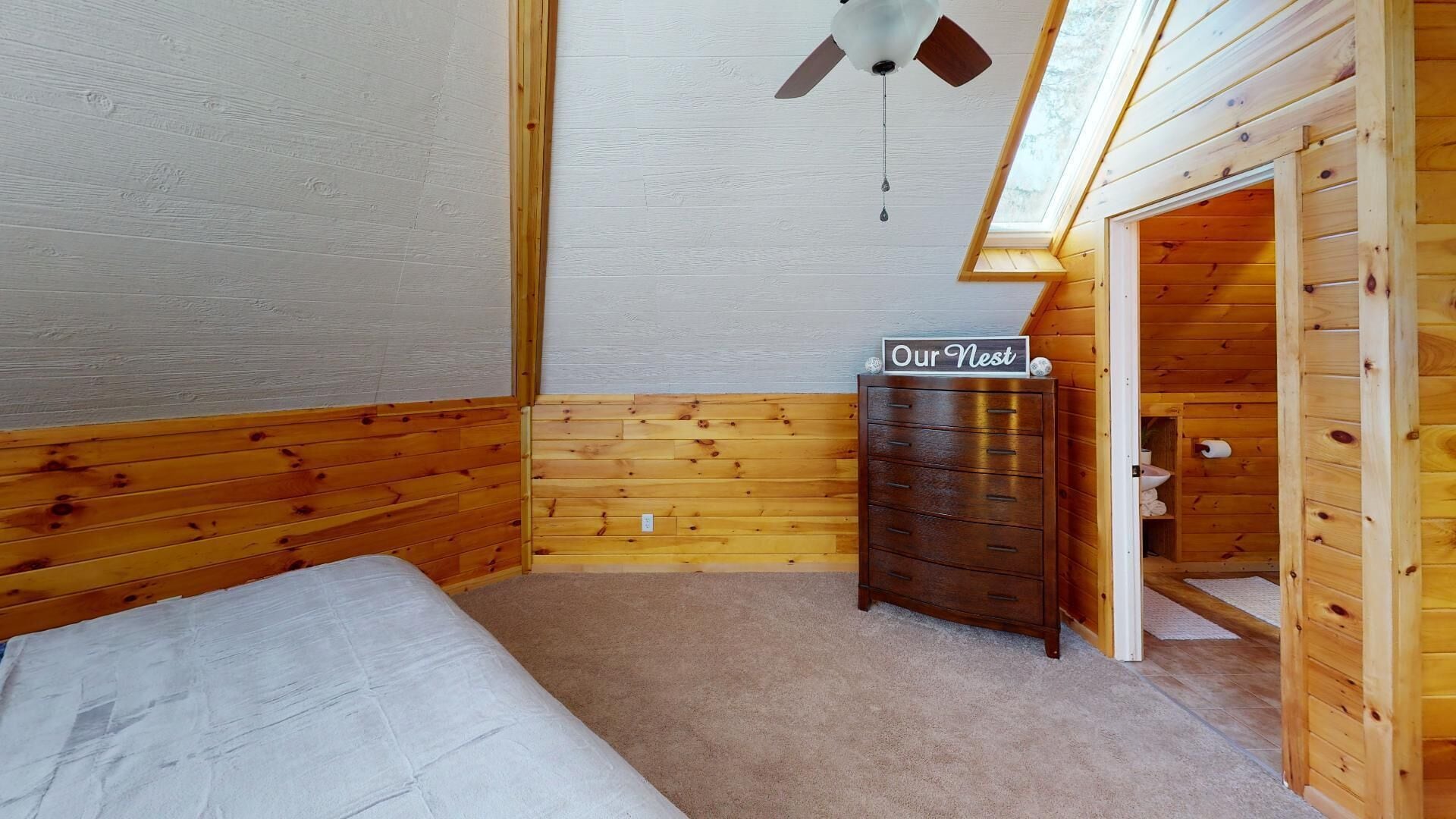 A room with a bed, a chest of drawers, a ceiling fan, and a skylight.