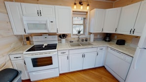 A compact kitchen with white cabinetry, a stove, a microwave, and a sink.