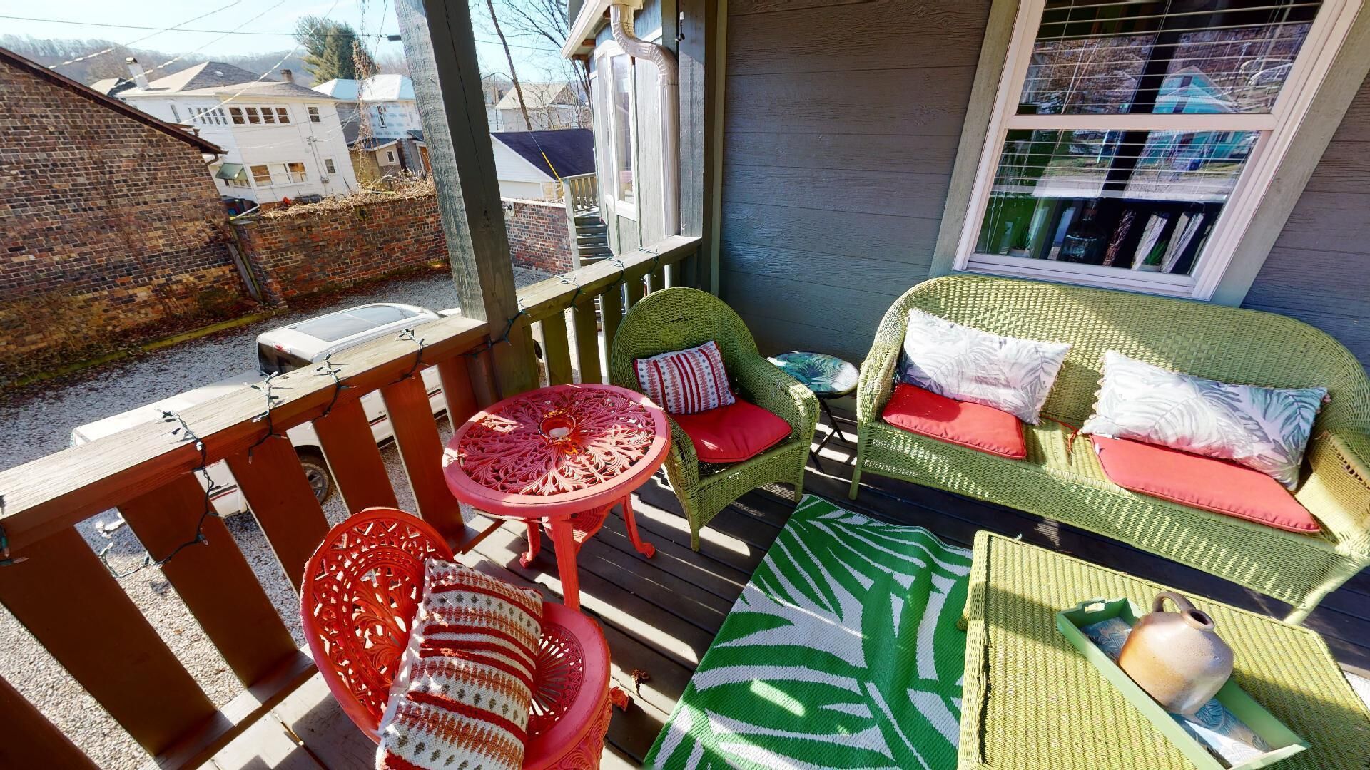 A covered outdoor seating area with wicker furniture and a table, a green sofa with red cushions, and a patterned rug.