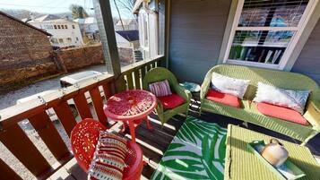 A covered outdoor seating area with wicker furniture and a table, a green sofa with red cushions, and a patterned rug.