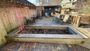 Un patio in legno con arredi da esterno, un'aiuola rialzata e un vialetto in mattoni.