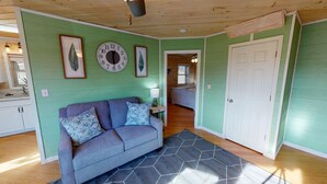A room with a green wall, a clock, a sofa with patterned cushions, and a door leading to another room. - Luxury Cottage in Nelsonville, close to Train, Opera House, near Hocking Hills (Nelsonville)
