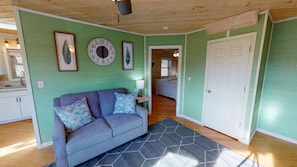 A room with a green wall, a clock, a sofa with patterned cushions, and a door leading to another room.