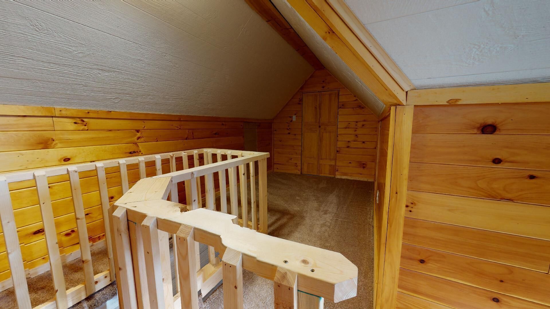 A wooden interior with a sloped ceiling, a wooden staircase, and a carpeted floor.