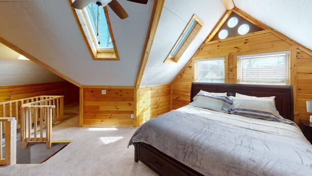 A bedroom with a sloped ceiling, wooden walls, a bed with pillows, a wooden crib, and skylights. - Luxury Cottage in Nelsonville, close to Train, Opera House, near Hocking Hills (Nelsonville)