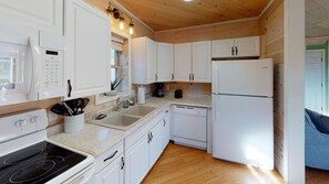 A compact kitchen with white cabinetry, a built-in oven, a refrigerator, and a coffee maker. - Luxury Cottage in Nelsonville near Hocking Hills (Nelsonville)