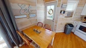 A cozy kitchen with wooden walls, a wooden dining table, and a trash bin. - Luxury Cottage in Nelsonville, close to Train, Opera House, near Hocking Hills (Nelsonville)