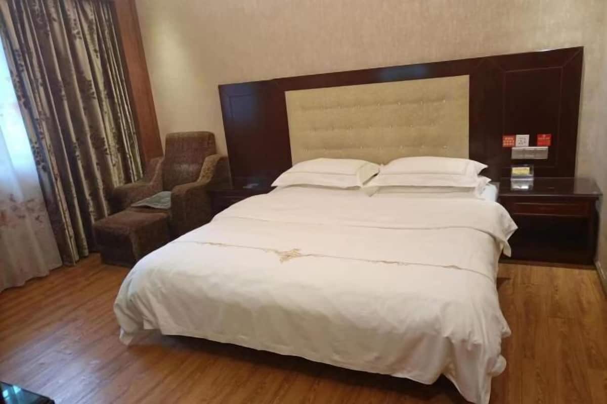 A hotel room with a large bed, a wooden headboard, a chair, a nightstand, and a curtain.