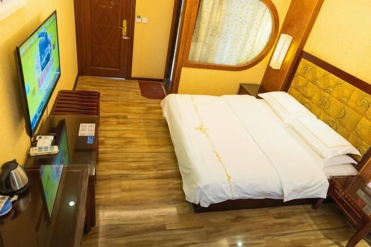 A hotel room with a bed, a TV on a stand, a desk with a telephone, and a wooden floor.