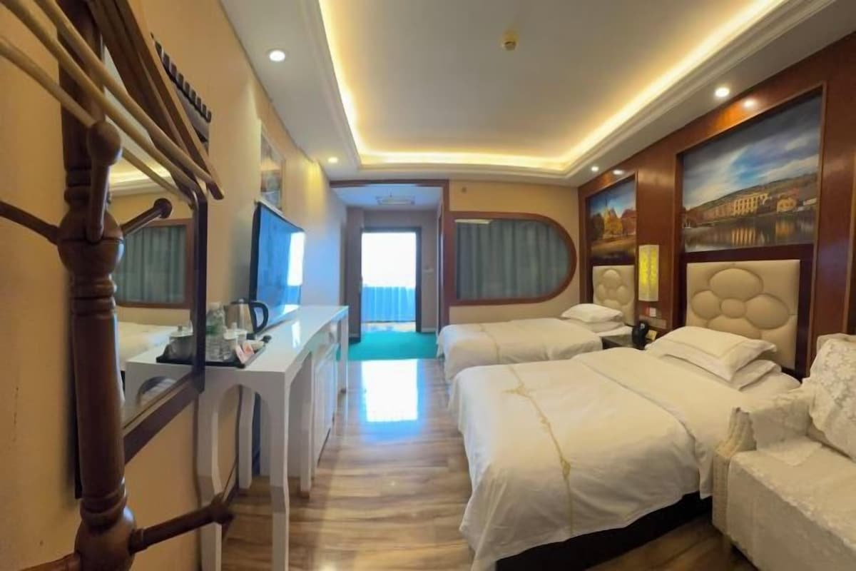 Una habitación de hotel con un escritorio, dos camas, un ventanal grande y un cuadro en la pared.