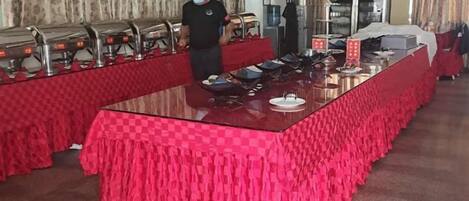 A buffet setup with a long table covered in a checkered tablecloth, surrounded by food service equipment.