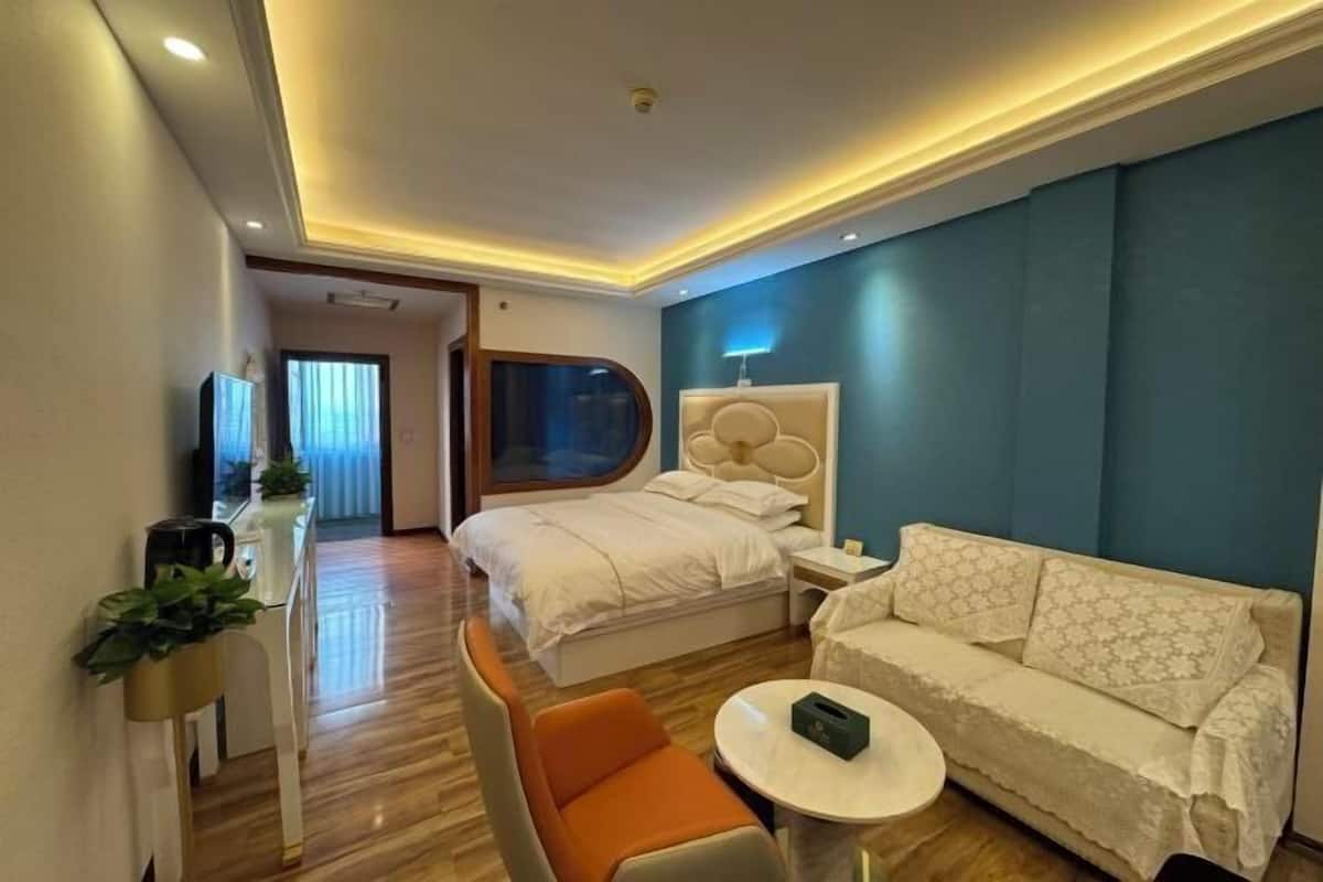 A modern hotel room with a bed, a sofa, a small table, and a TV.