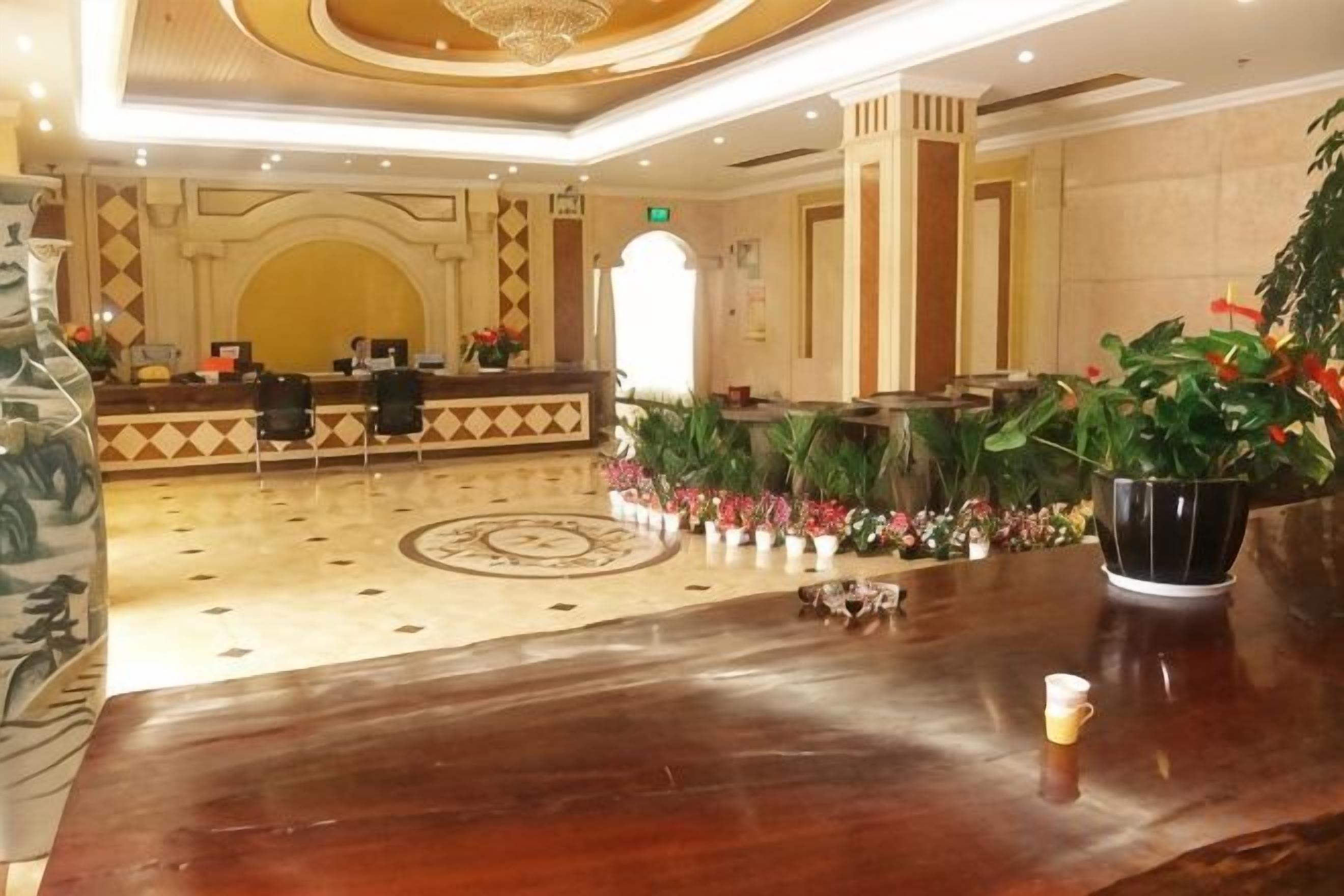 A hotel lobby with a reception desk, seating area, and decorative plants.