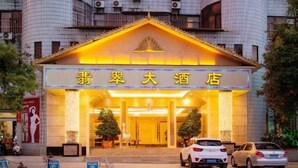 A hotel entrance with a sign in Chinese characters, two potted plants, and two cars parked in front. - Feicui Hotel (Mangshi)