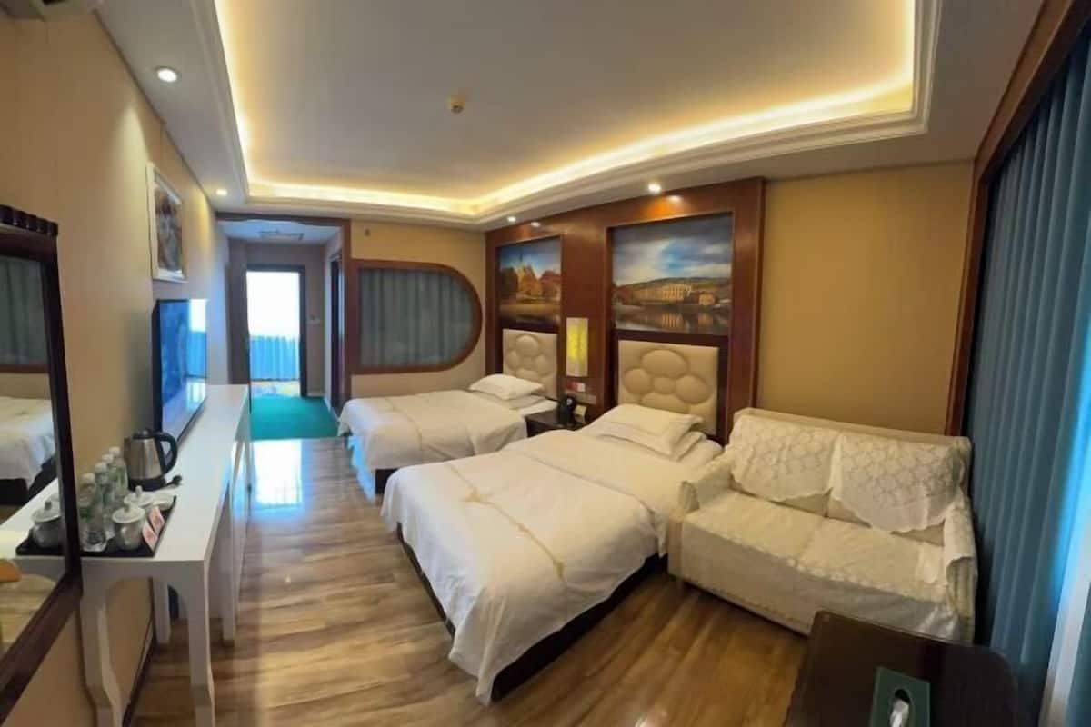 A hotel room with two beds, a sofa, a desk with a tray of toiletries, and a painting on the wall.