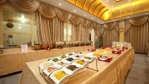 A buffet setup with various food items in bowls, a long table covered with a beige tablecloth, and a ceiling with a golden design. - Feicui Hotel (Mangshi)