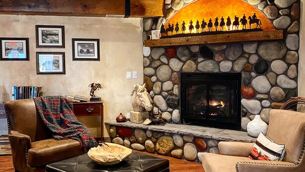 A cozy living room with a stone fireplace, leather furniture, and framed pictures on the wall. - River Rock Inn B&B - Adults Only (Green River)