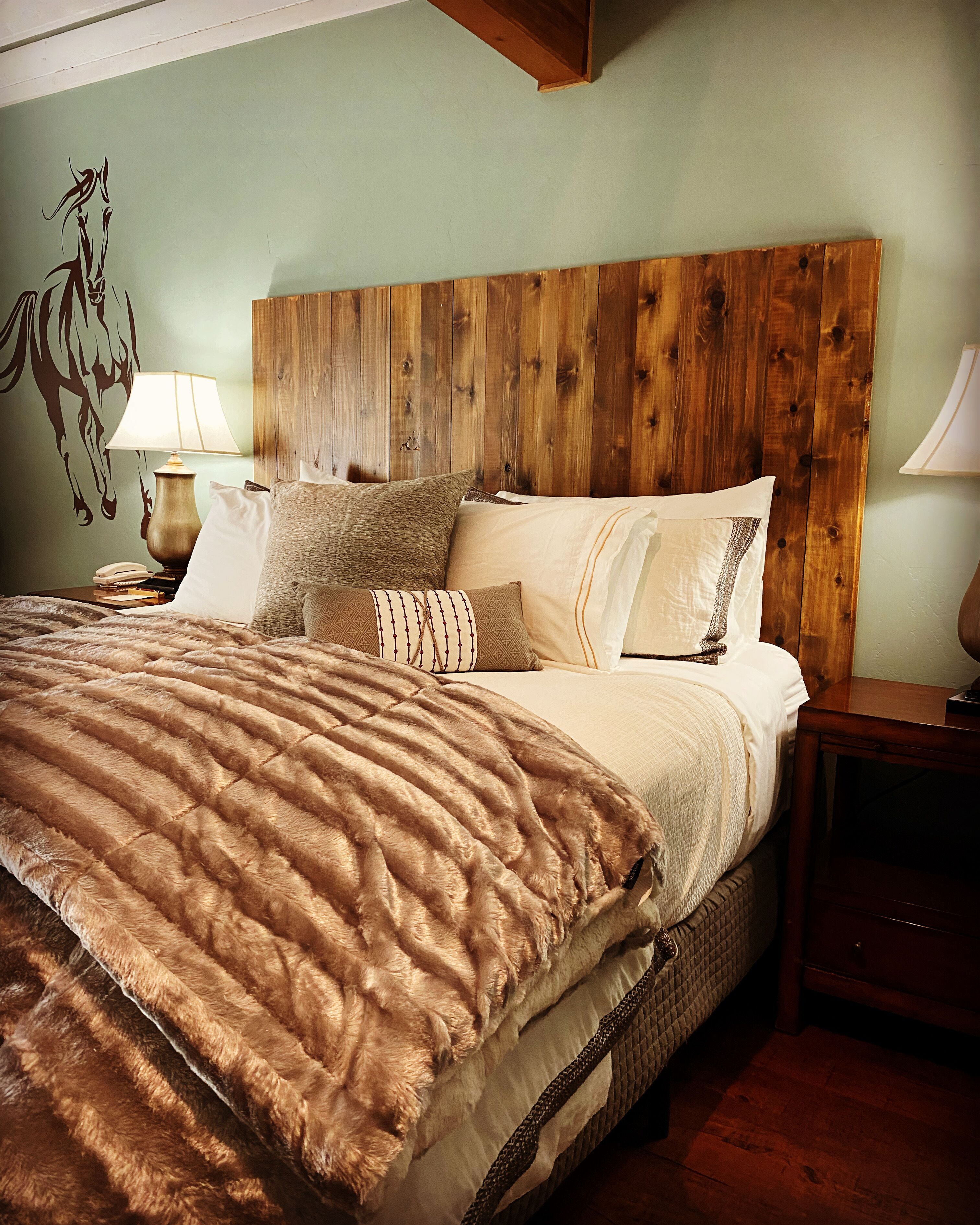 Un dormitorio con cabecera de madera, una cama grande con muchas almohadas, una mesita de noche con una lámpara y un teléfono instalado en la pared.