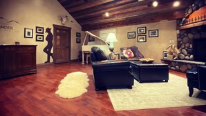 A spacious living room with a high ceiling, wooden beams, a fireplace, and a stone wall. - River Rock Inn B&B - Adults Only (Green River)