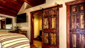A bedroom with a bed, a dresser, a mirror, a television, and a wooden door. - River Rock Inn B&B - Adults Only (Green River)
