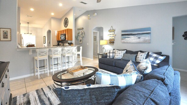 A living room with a dark blue sofa, a round coffee table, and a kitchen area in the background.